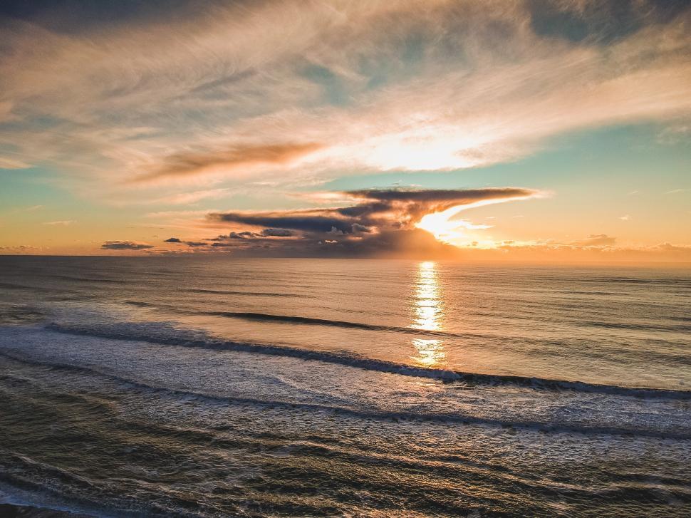 Free Image of Sunset over calm ocean waves near the coast with dramatic cloud formations 