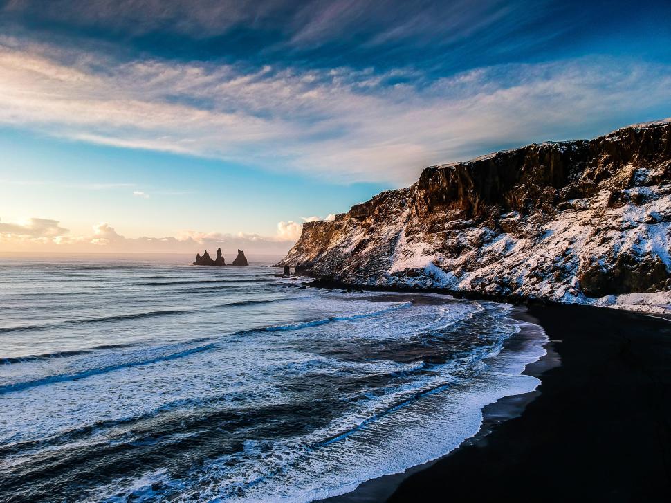 Free Image of Breathtaking coastal view of black sand beach and rocky formations at sunset 