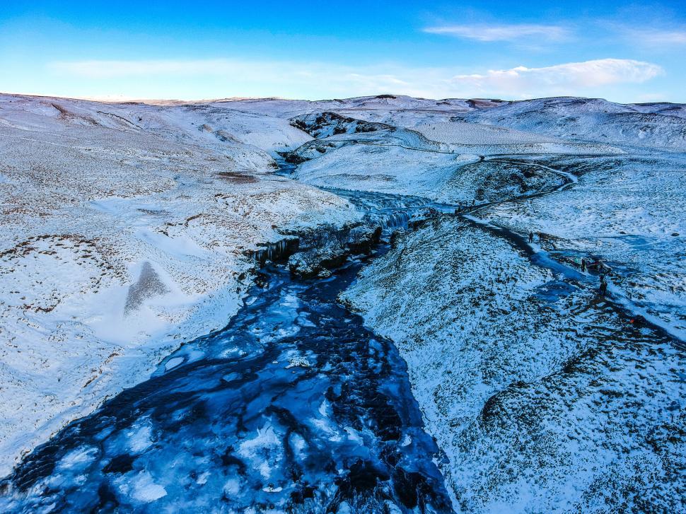 Free Image of Winter landscape in Iceland featuring a frozen river and snow-covered hills 