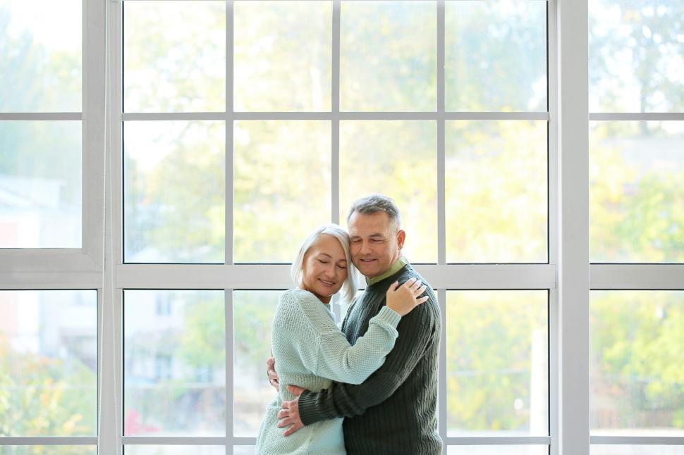 Free Image of Elderly couple embraces by a large window in bright light 