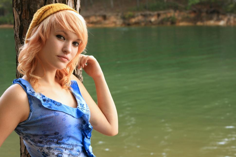 Free Image of A beautiful young woman posing against a tree by a lake 