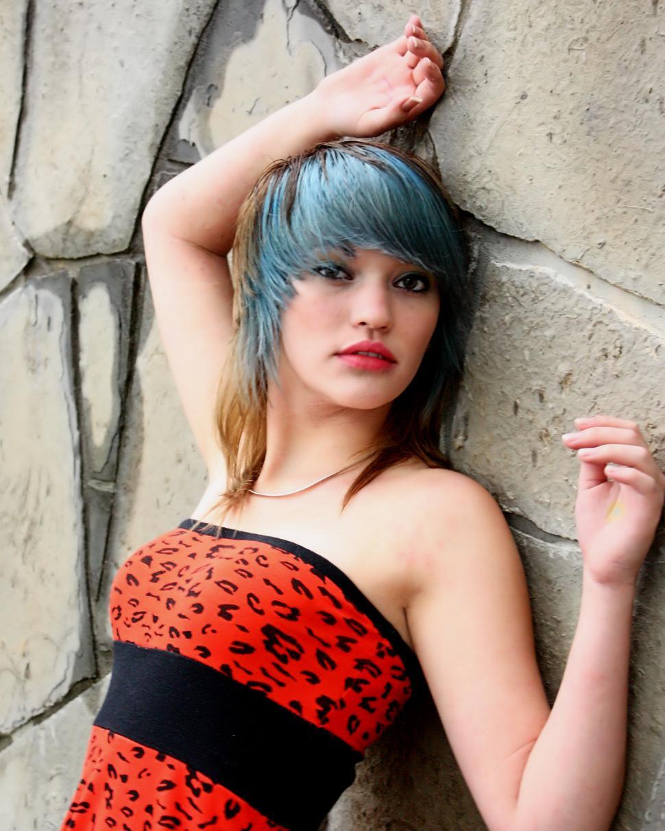 Free Image of A beautiful young woman posing in a red dress against a stone wall 