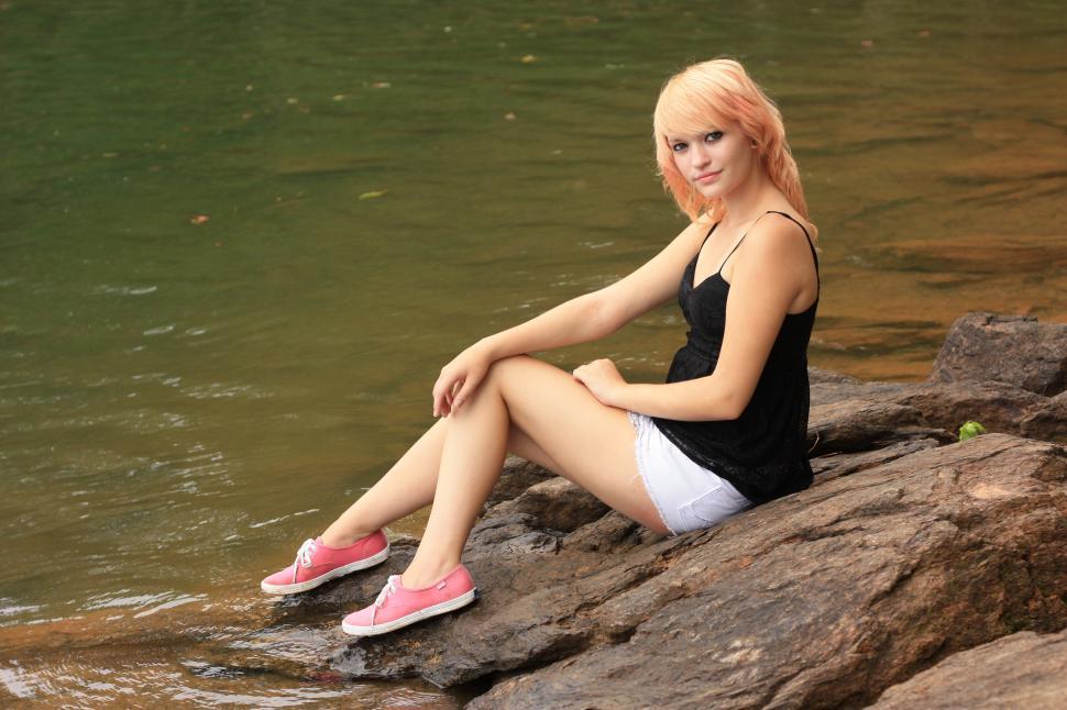 Free Image of A beautiful young woman posing on a rock by a lake 