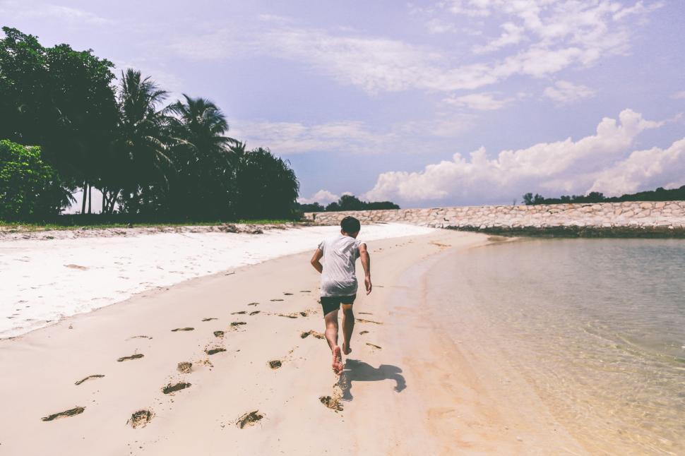 Free Image of Man Walking Along Sandy Beach Next to Ocean 