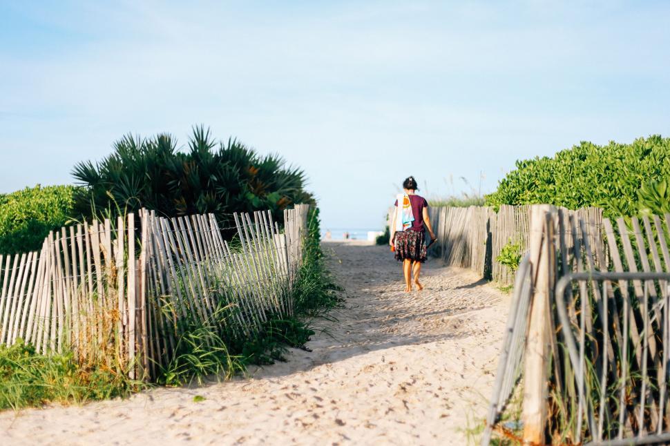 Free Image of Person Walking Down a Dirt Road Next to a Fence 