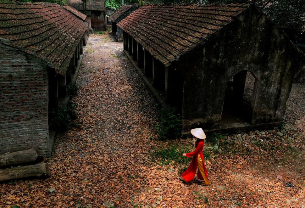 Free Image of Woman in Red Dress and White Hat Walking Through Village 