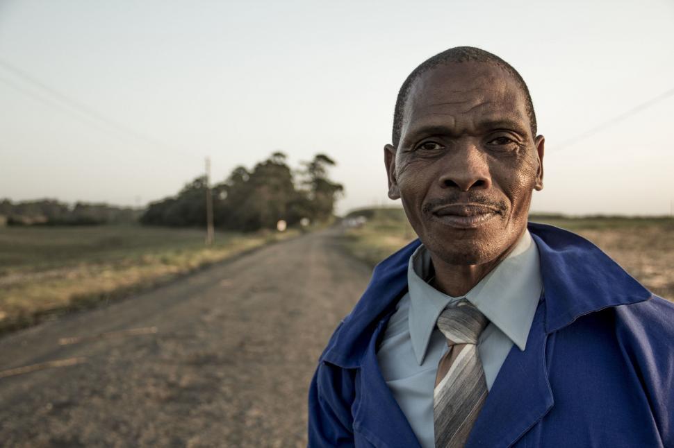 Free Image of Man in Blue Jacket and Tie Standing on Dirt Road 