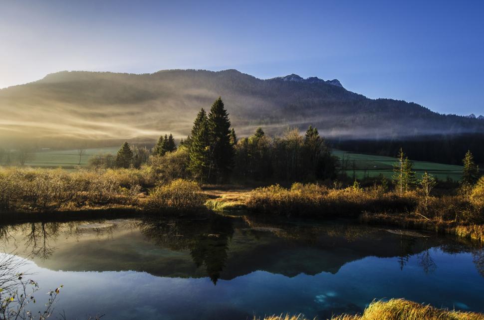 Free Image of Small Pond in Grassy Field With Mountain in Background 