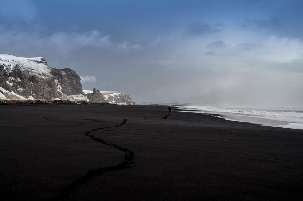 Free Image of Person Walking on Beach With Mountain in Background 