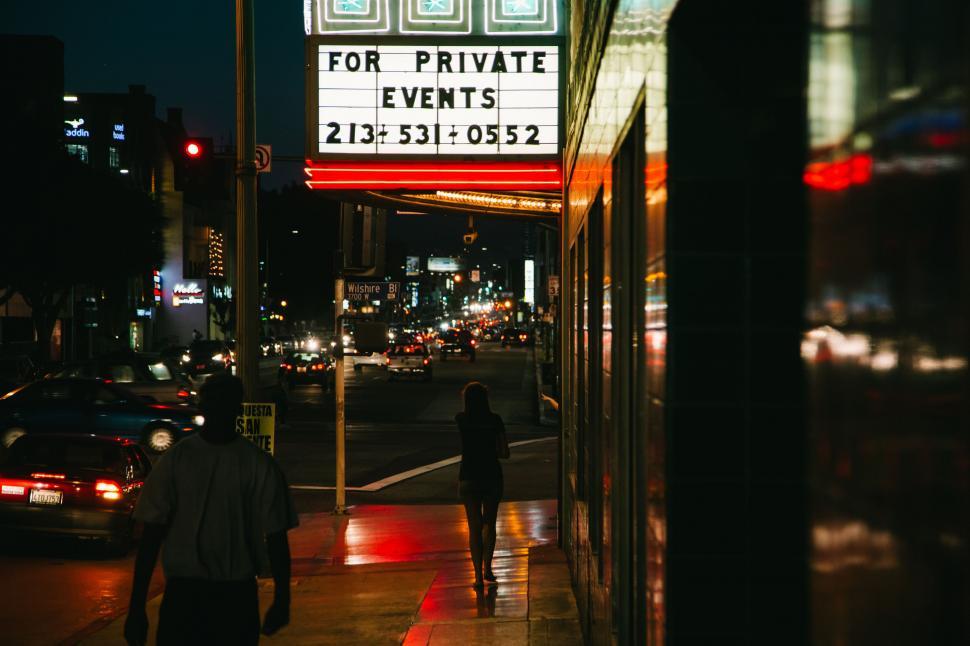 Free Image of Couple Walking Down Street Next to Theater Sign 