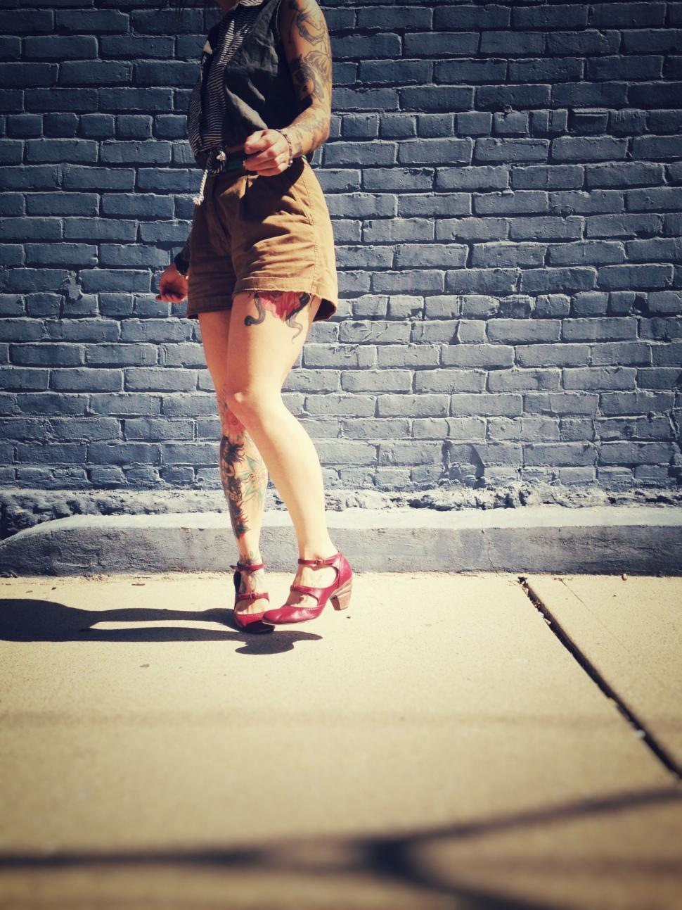 Free Image of Woman With Tattoos Standing on Sidewalk 