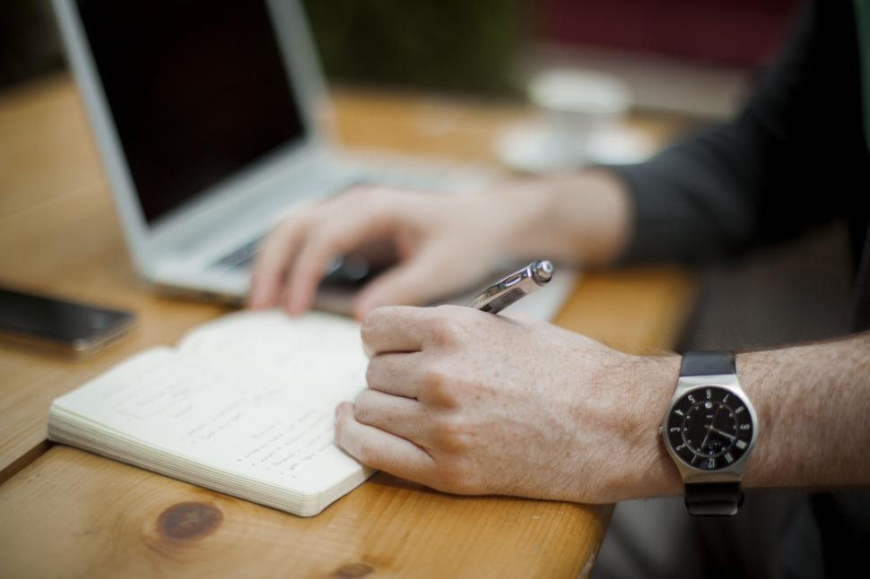 Free Image of Man Sitting at Desk Writing on Notepad 