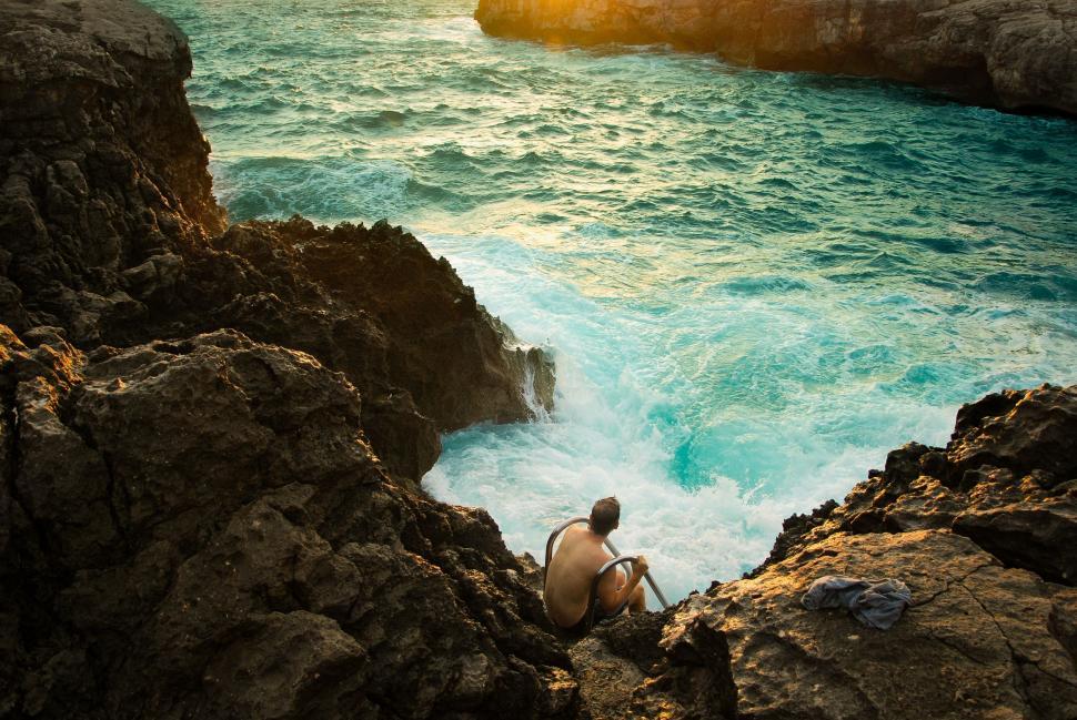 Free Image of Person Sitting on Rock by Ocean 