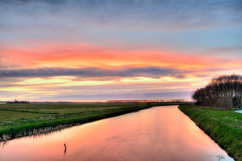 Free Image of River Flowing Through Lush Green Field Under Cloudy Sky 