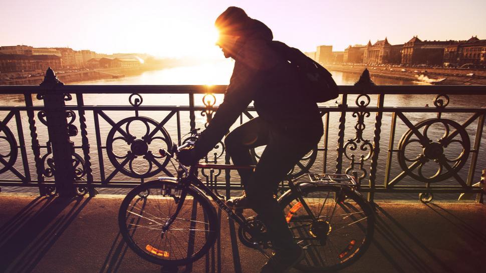 Free Image of Man Riding Bike Down Street Next to Bridge 