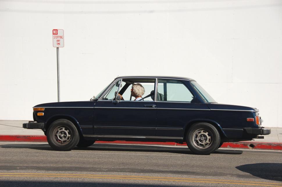 Free Image of Black Car Driving Down Street Next to White Wall 