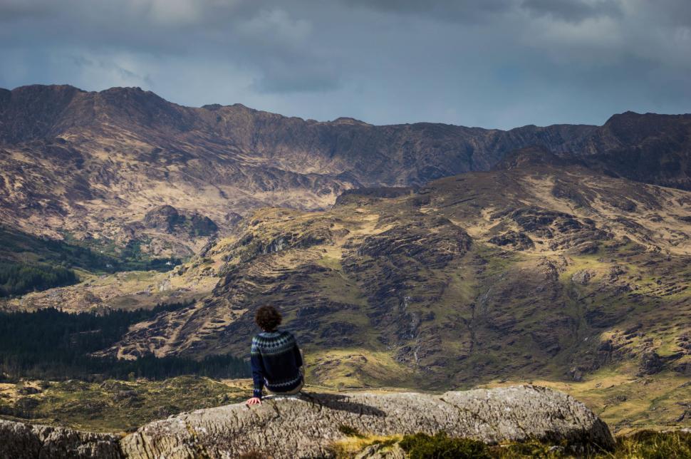 Free Image of Person Sitting on a Rock With Mountains in Background 