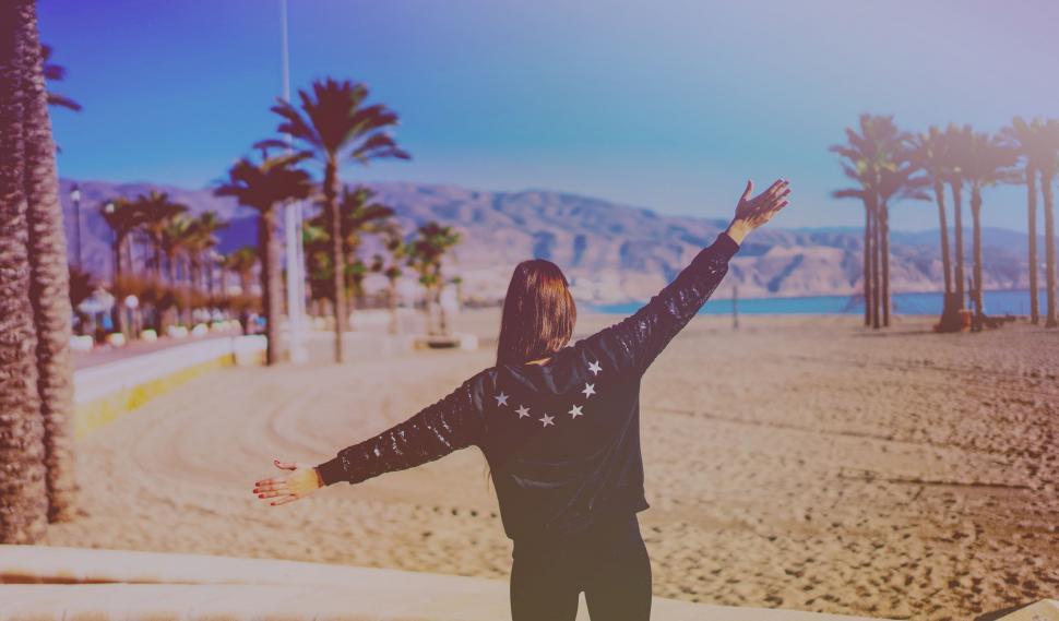 Free Image of Person Standing on Beach With Arms Raised 