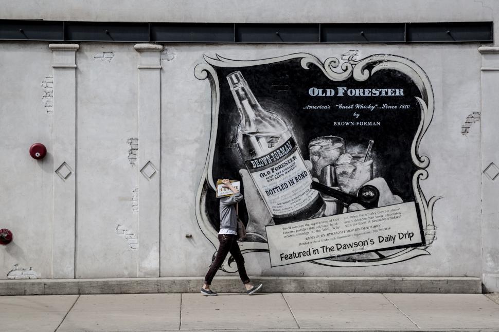 Free Image of Man Walking Past Poster on Side of Building 