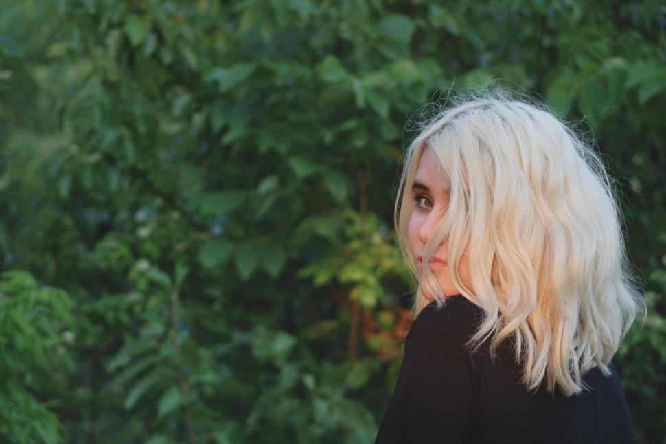 Free Image of Woman With Blonde Hair Standing in Front of Trees 