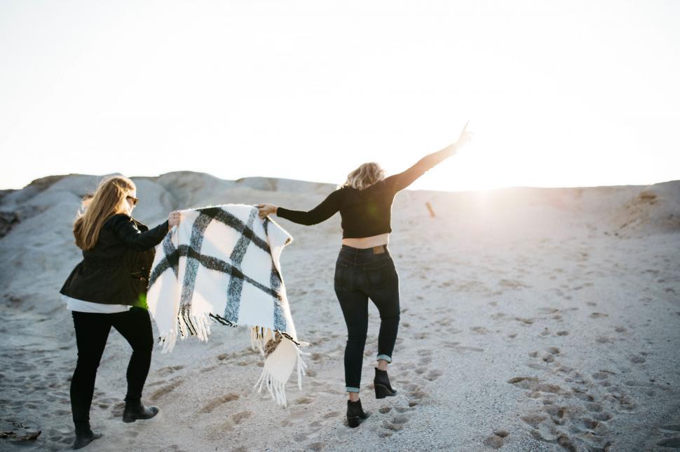 Free Image of Two Women Standing in the Sand Holding a Blanket 