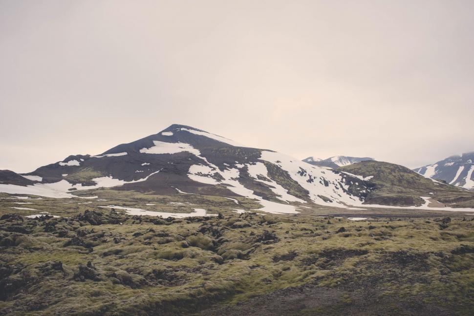 Free Image of Snow-covered Mountain With Grass Under Cloudy Sky 