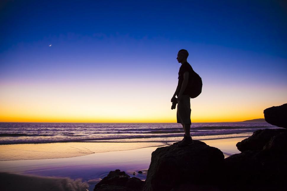 Free Image of Man Standing on Top of Rock by Ocean 