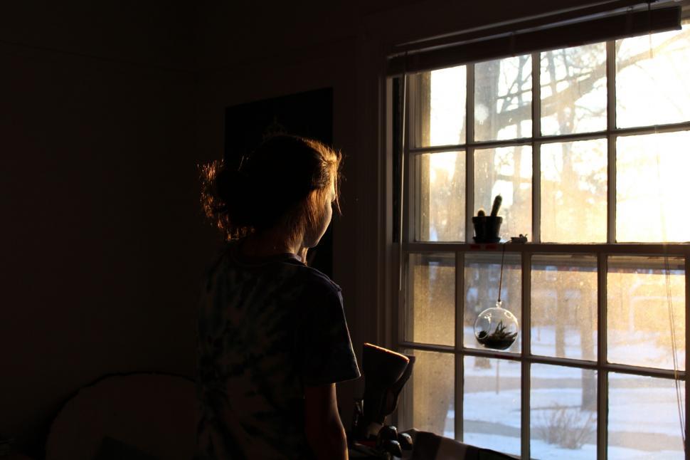 Free Image of Woman Looking Out Window at Snow Covered Yard 
