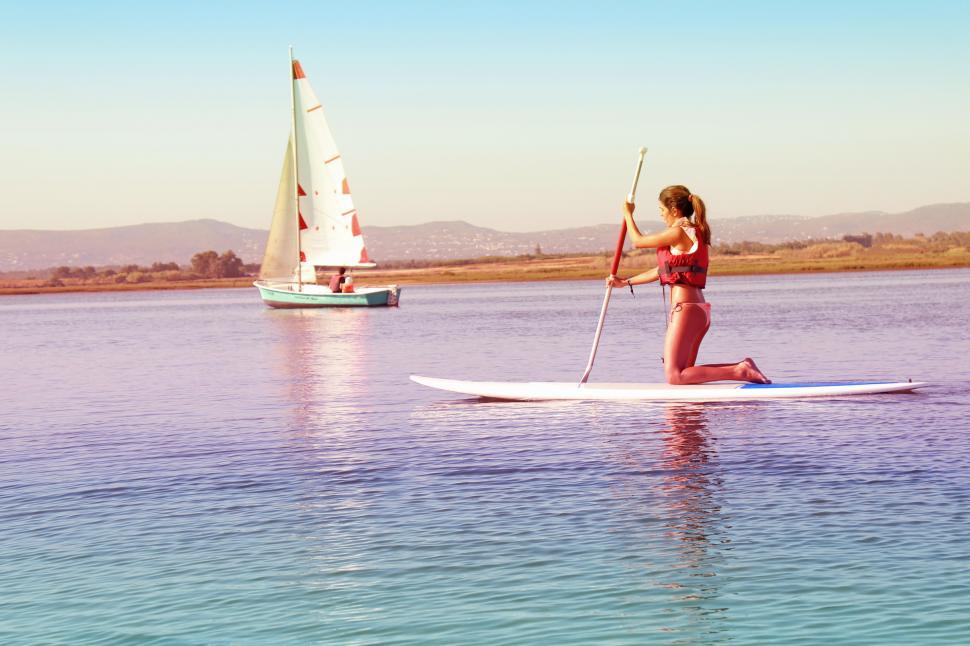 Free Image of Watersports - Girl Practicing on Paddle Board with Sail Boat on  