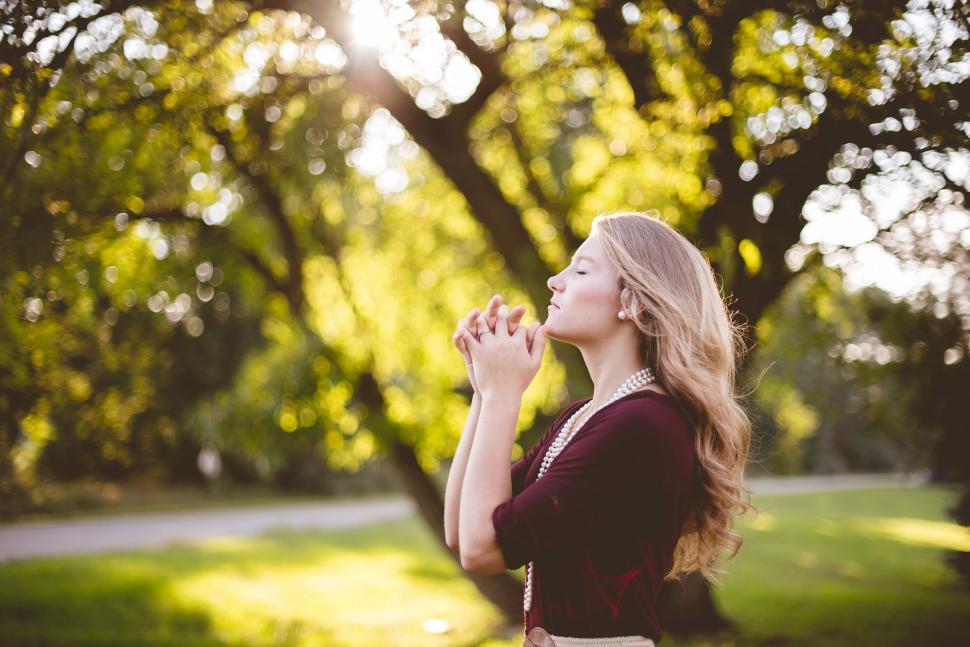 Free Image of Woman Standing in Front of Tree With Hands Together 