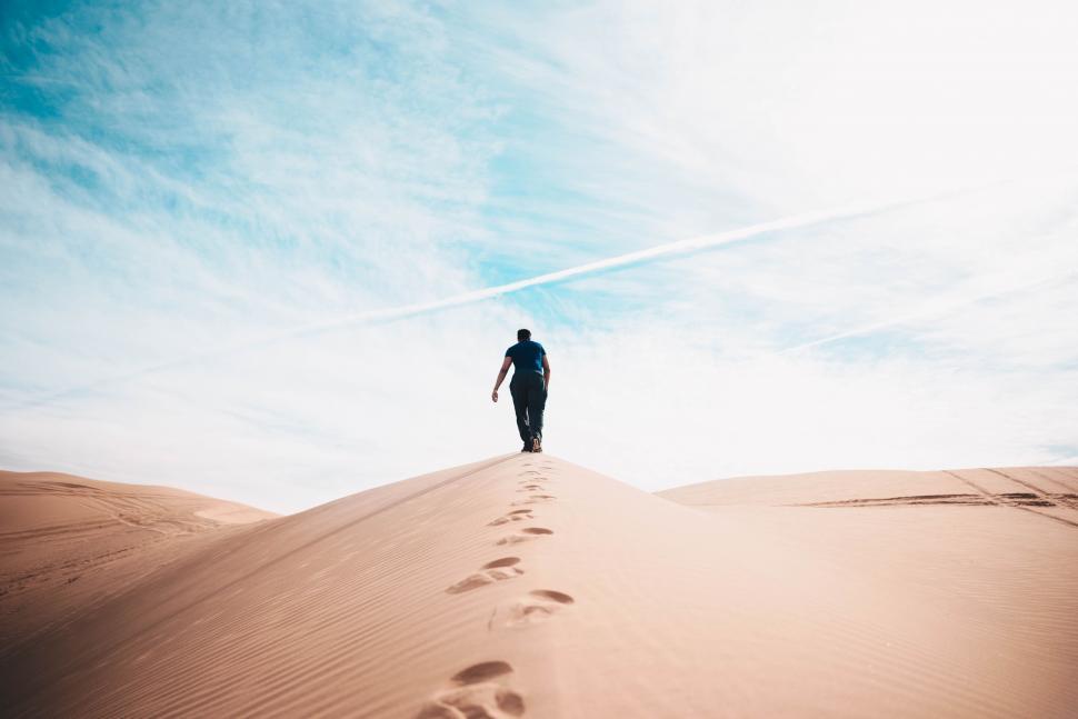 Free Image of Man Walking Across Sandy Beach Under Blue Sky 