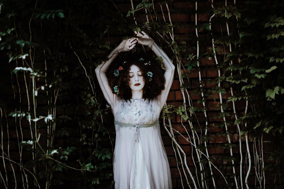 Free Image of Woman in White Dress Standing in Front of Brick Wall 
