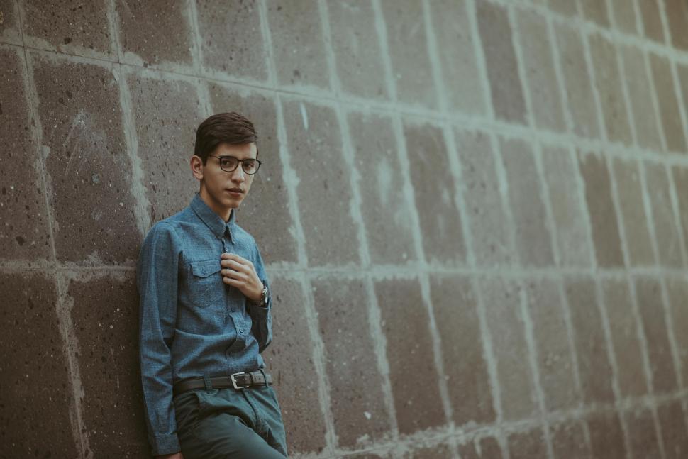 Free Image of Man Leaning Against Brick Wall Wearing Glasses 