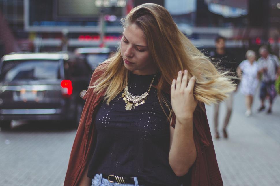 Free Image of Woman Walking Down Street With Wind-Blown Hair 