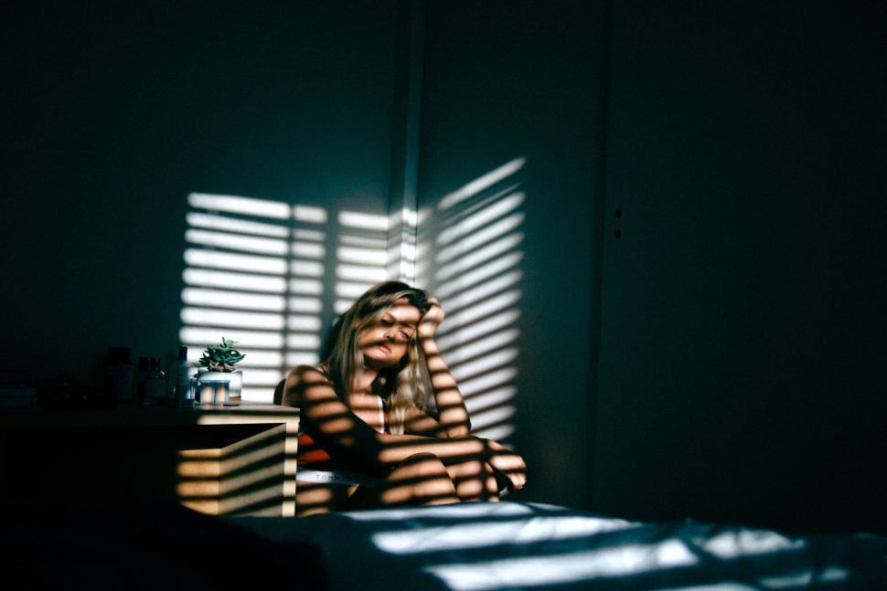 Free Image of Woman Sitting on Bed in Dark Room 