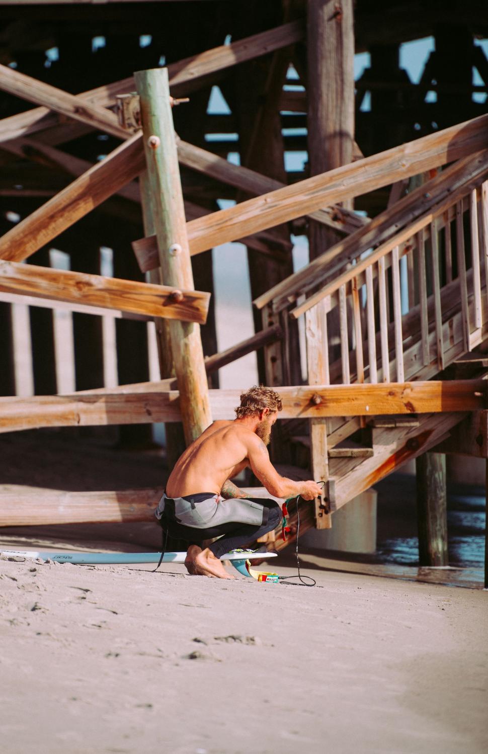 Free Image of Shirtless Man Kneeling on Beach Next to Surfboard 