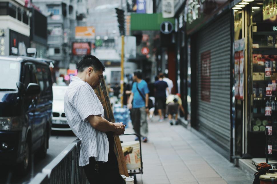 Free Image of Man Standing on Sidewalk Looking at Cell Phone 