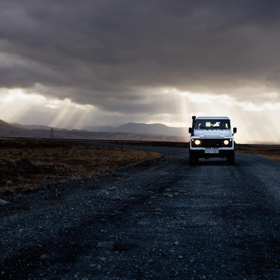 Free Image of White Truck Driving Down Dirt Road Under Cloudy Sky 