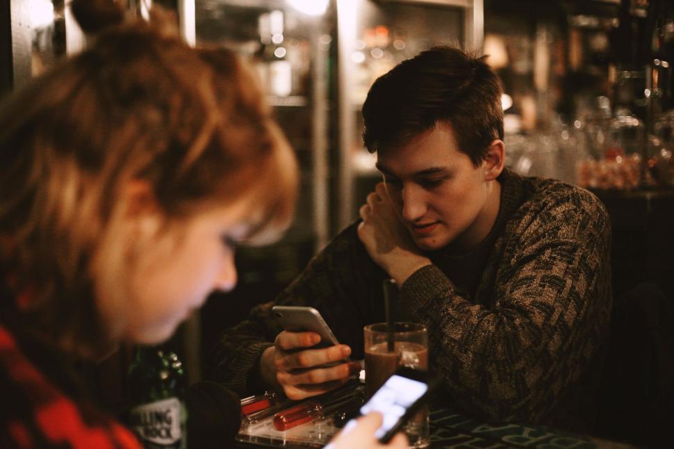 Free Image of Man and Woman Sitting at Table Looking at Cell Phone 