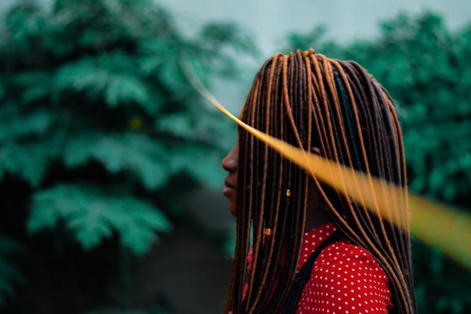 Free Image of Woman With Long Dreadlocks Standing in Front of Trees 