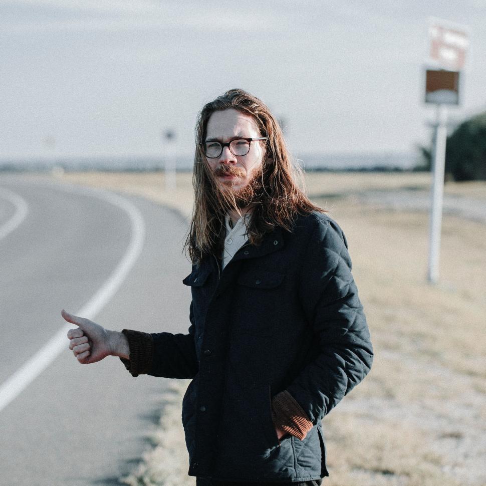 Free Image of Man With Long Hair and Glasses Standing on Side of Road 