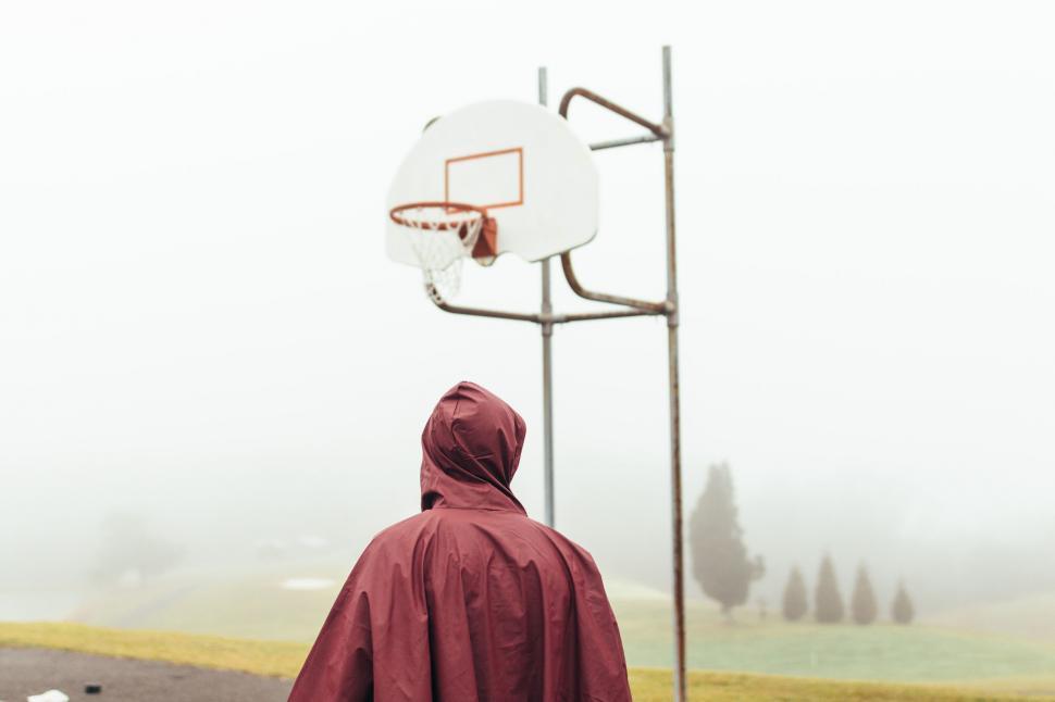 Free Image of Person in a Red Poncho Standing Next to a Basketball Hoop 