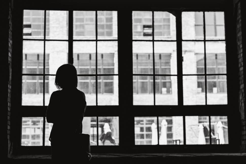 Free Image of Woman Standing in Front of Window With Suitcase 