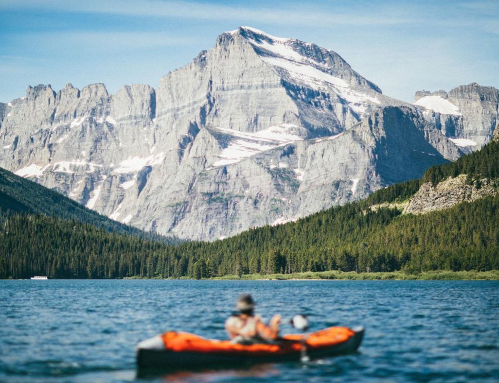 Free Image of Person Rafting on Orange Raft in Lake With Mountain Background 