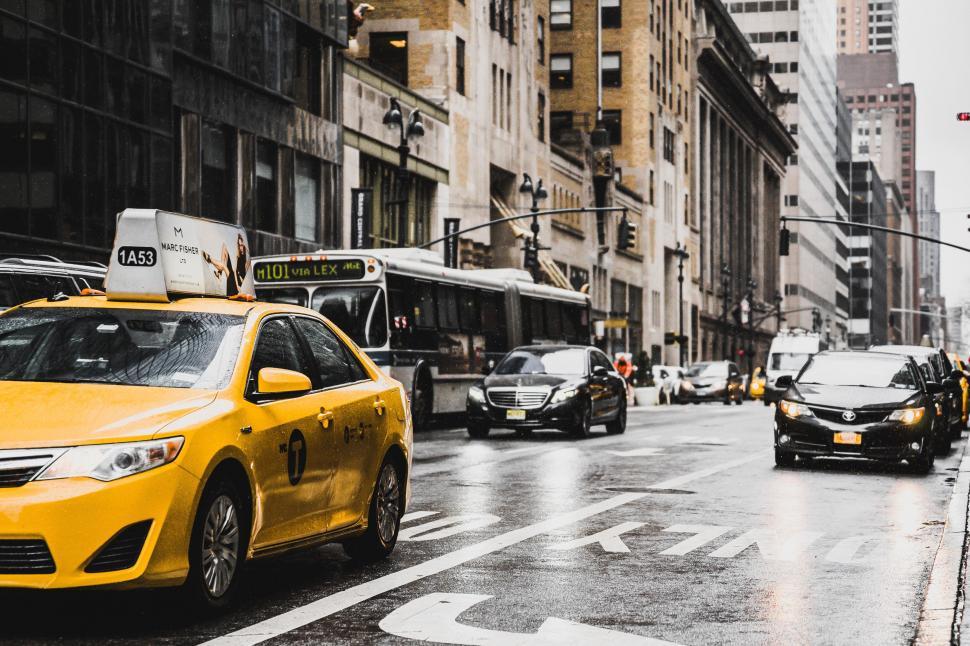 Free Image of Yellow Taxi Cab Driving Down Street Next to Tall Buildings 