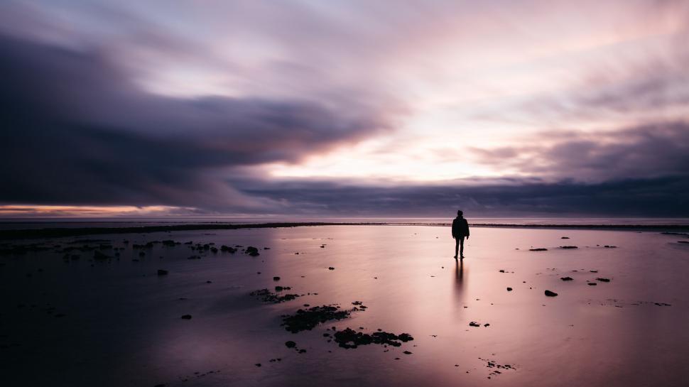 Free Image of Person Standing on Wet Beach Under Cloudy Sky 