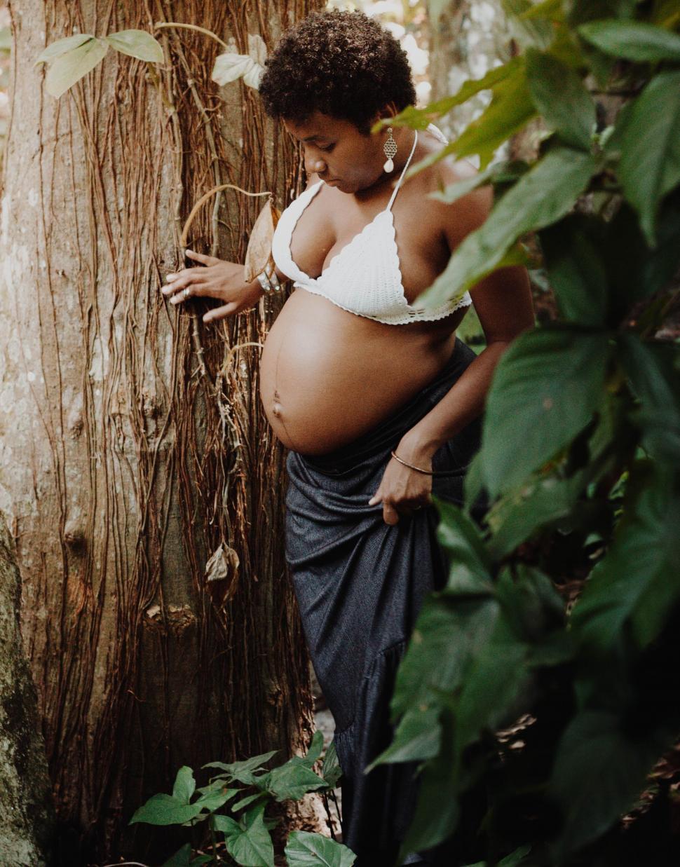 Free Image of Pregnant Woman Leaning Against Tree in Forest 