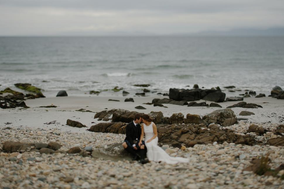 Free Image of Bride and Groom Sitting on Rocky Beach 