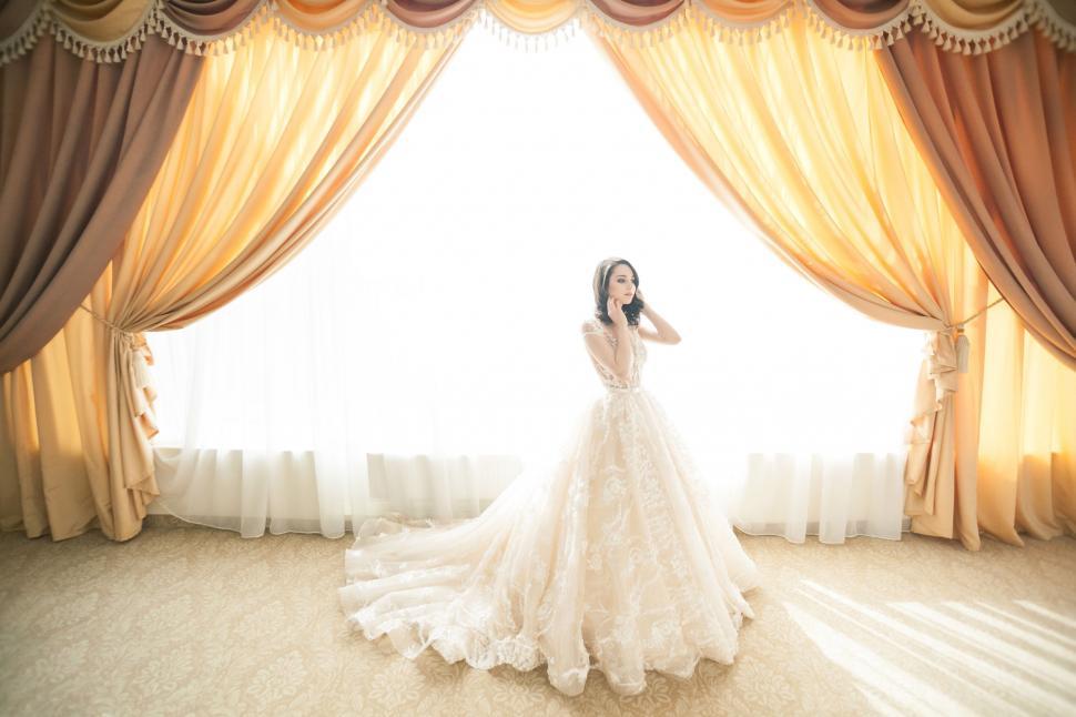 Free Image of Bride in Wedding Dress Standing in Front of Window 