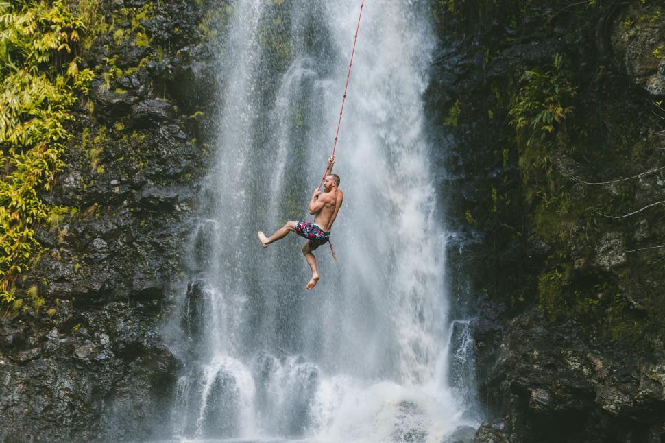 Free Image of Man Hanging Onto Rope in Front of Waterfall 